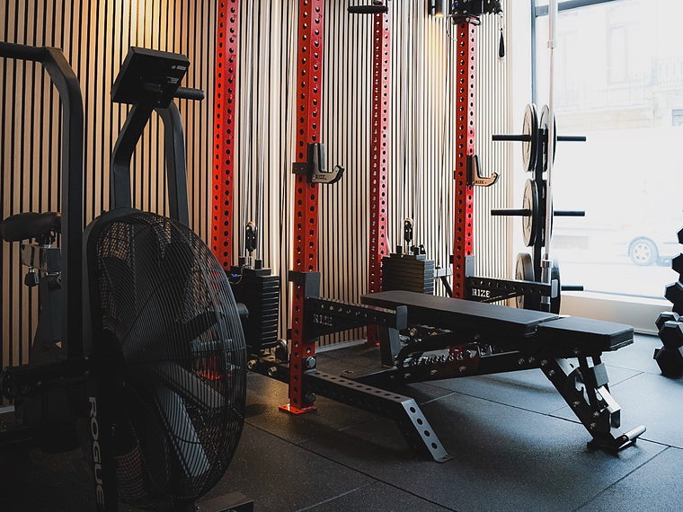 Le studio&nbsp;: rack de musculation rouge, banc et vélo à air devant un mur en tasseaux de bois