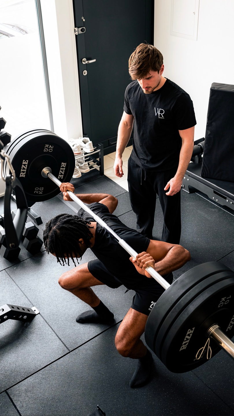 Au studio, un coach d’Aesthetic Studio corrige le squat barre de son client